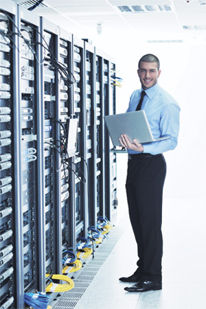 man holding a laptop and standing next to servers